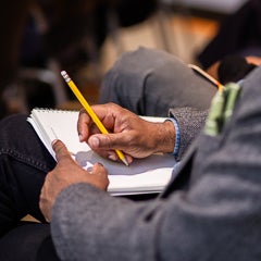 Event attendee writing with a pencil in a notebook